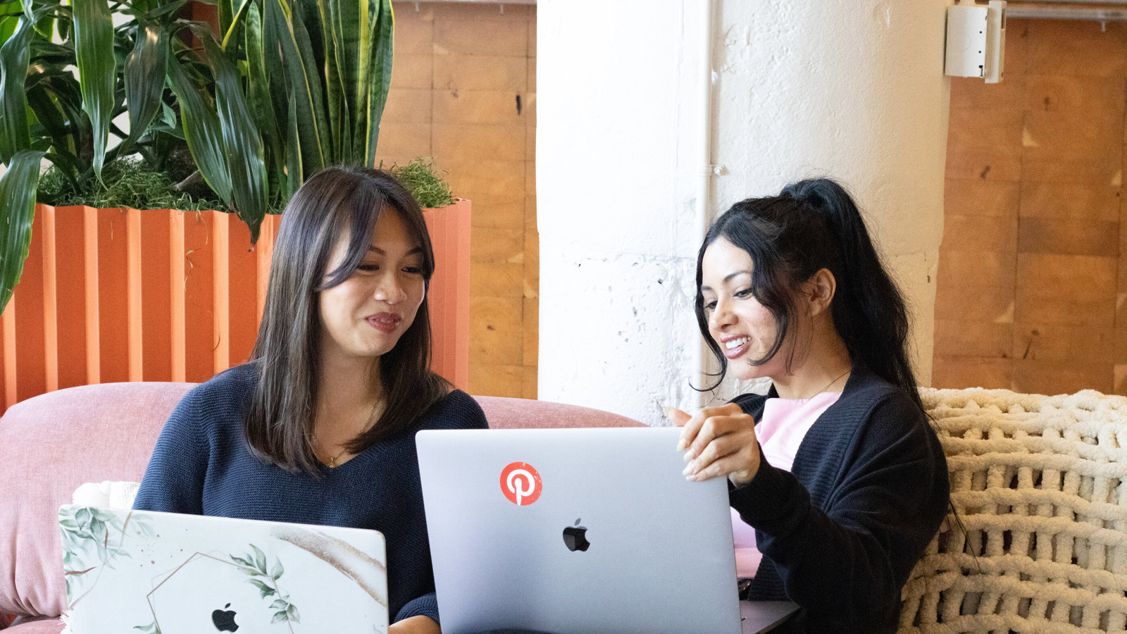 two women sitting on a couch with laptops
