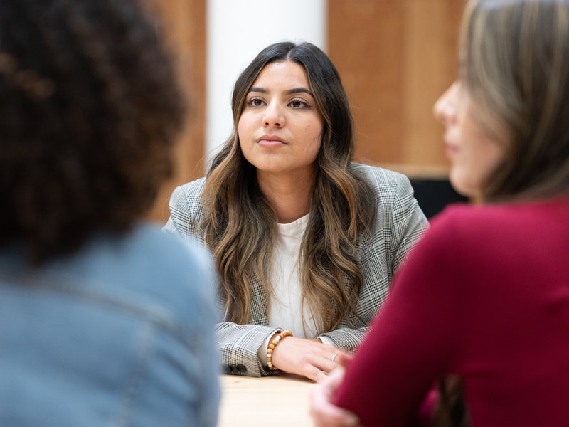 a woman sitting at a table with other people in the background
